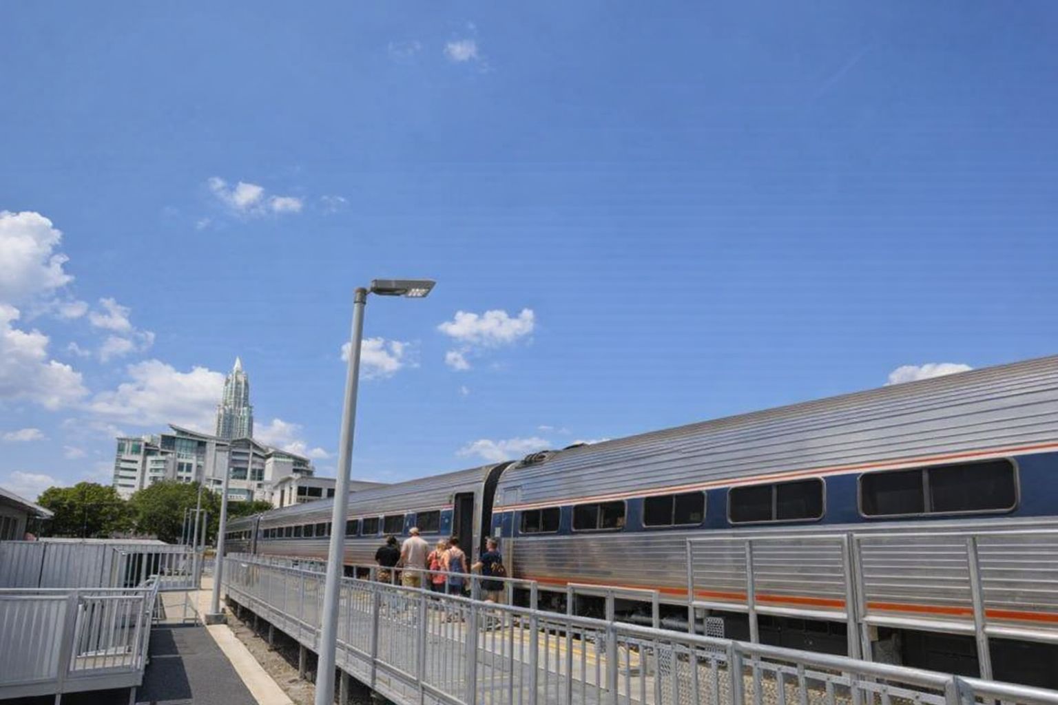 Reisende steigen an einem Bahnhof in einen silbernen Reisezug ein.