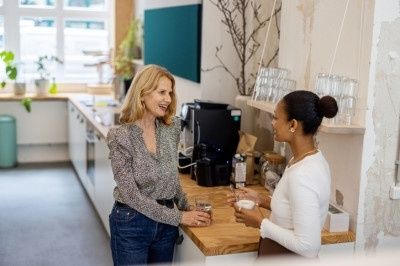 Zwei Kolleginnen unterhalten sich bei einer Kaffeepause in der Büroküche