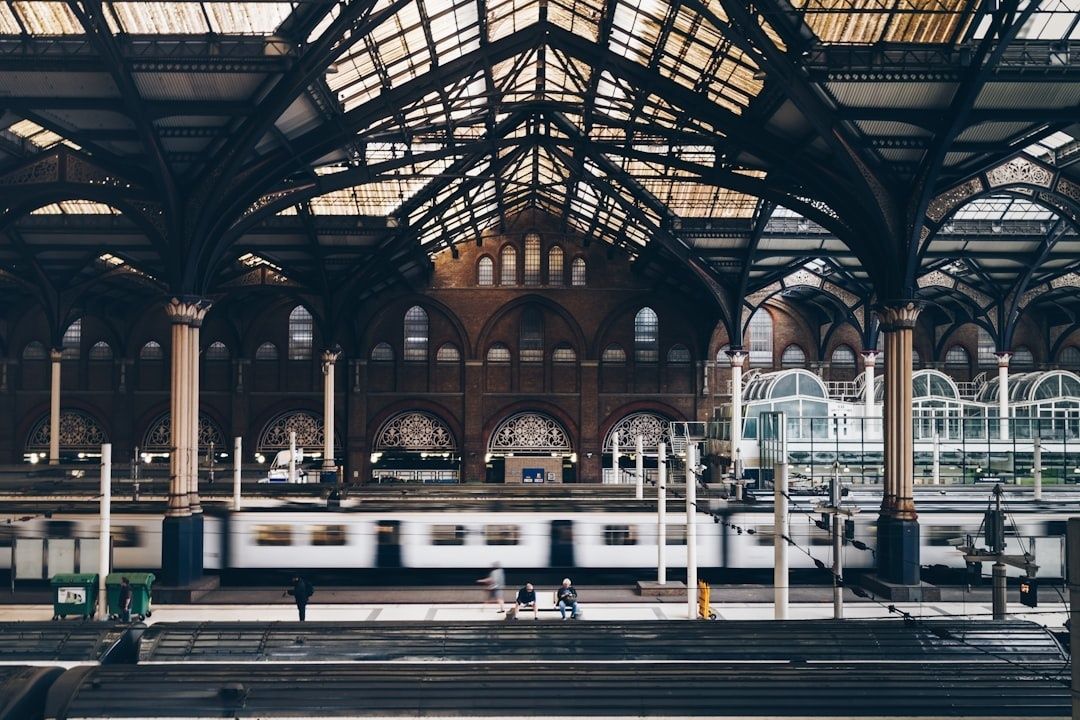 Historische Bahnhofshalle mit vorbeifahrendem Zug und wartenden Reisenden